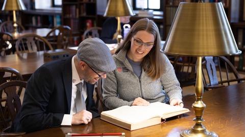 Two people read a large book together.