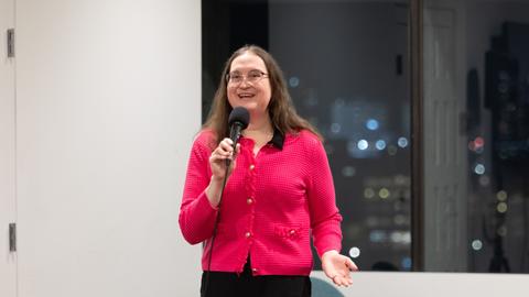 A woman speaks enthusiastically into a microphone.