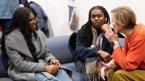 Three women have a conversation on a couch.