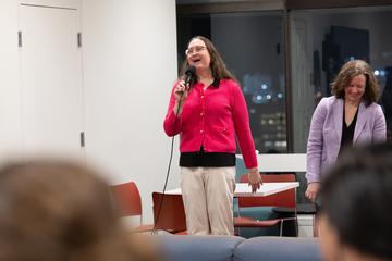 A teach speaks into a microphone in front of an assembly.