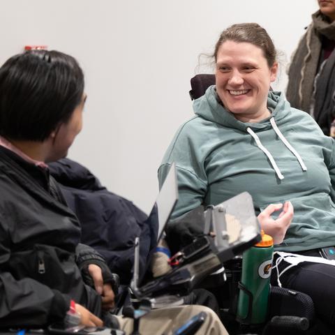 Two people in motorized wheelchairs are having a lively conversation.