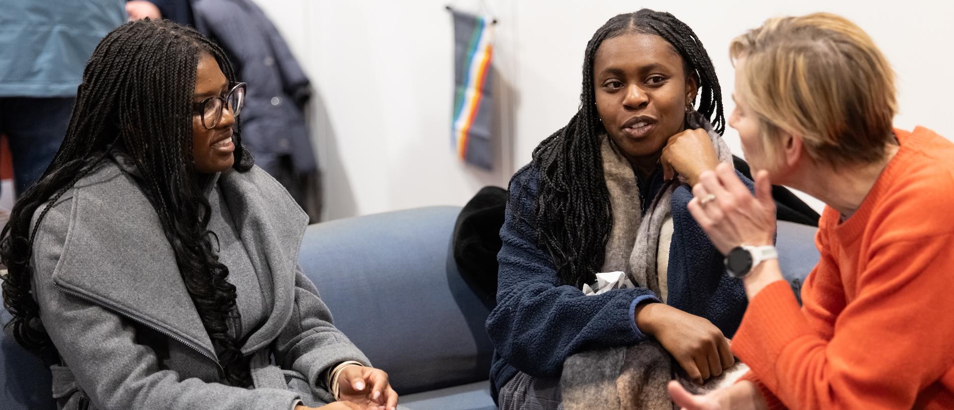 Three women have a conversation on a couch.